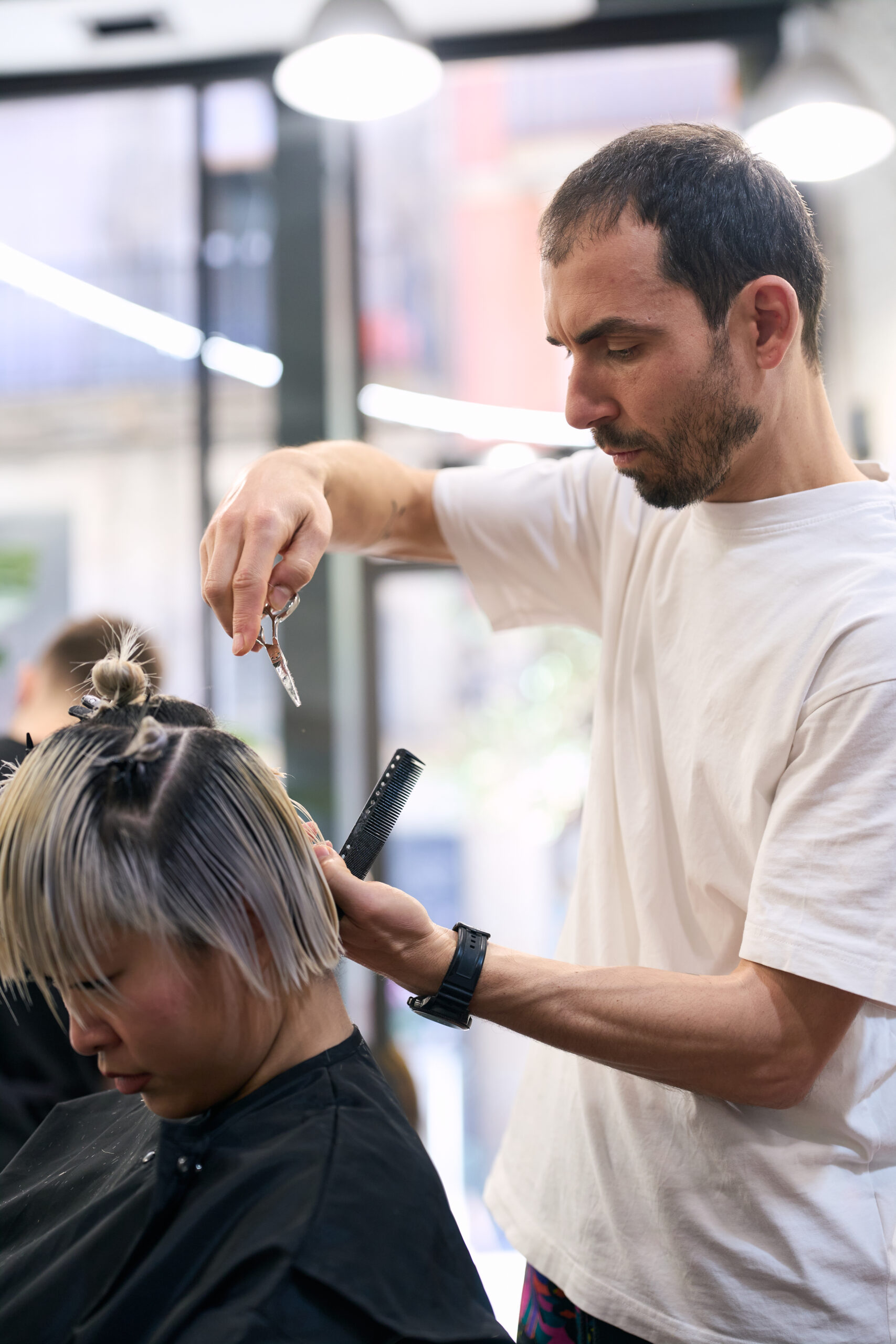 Professional male hairdresser cutting hair of young female client with short dyed hair in modern hair salon