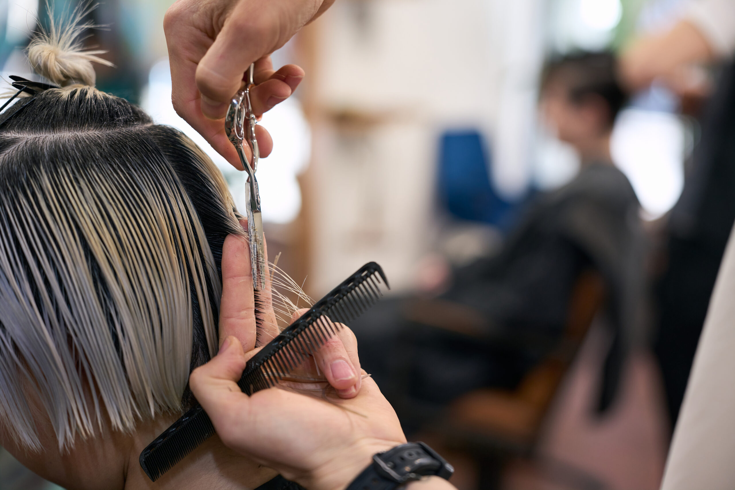 Hairdresser cutting hair tips of young female model with comb and scissors in hairdressing salon