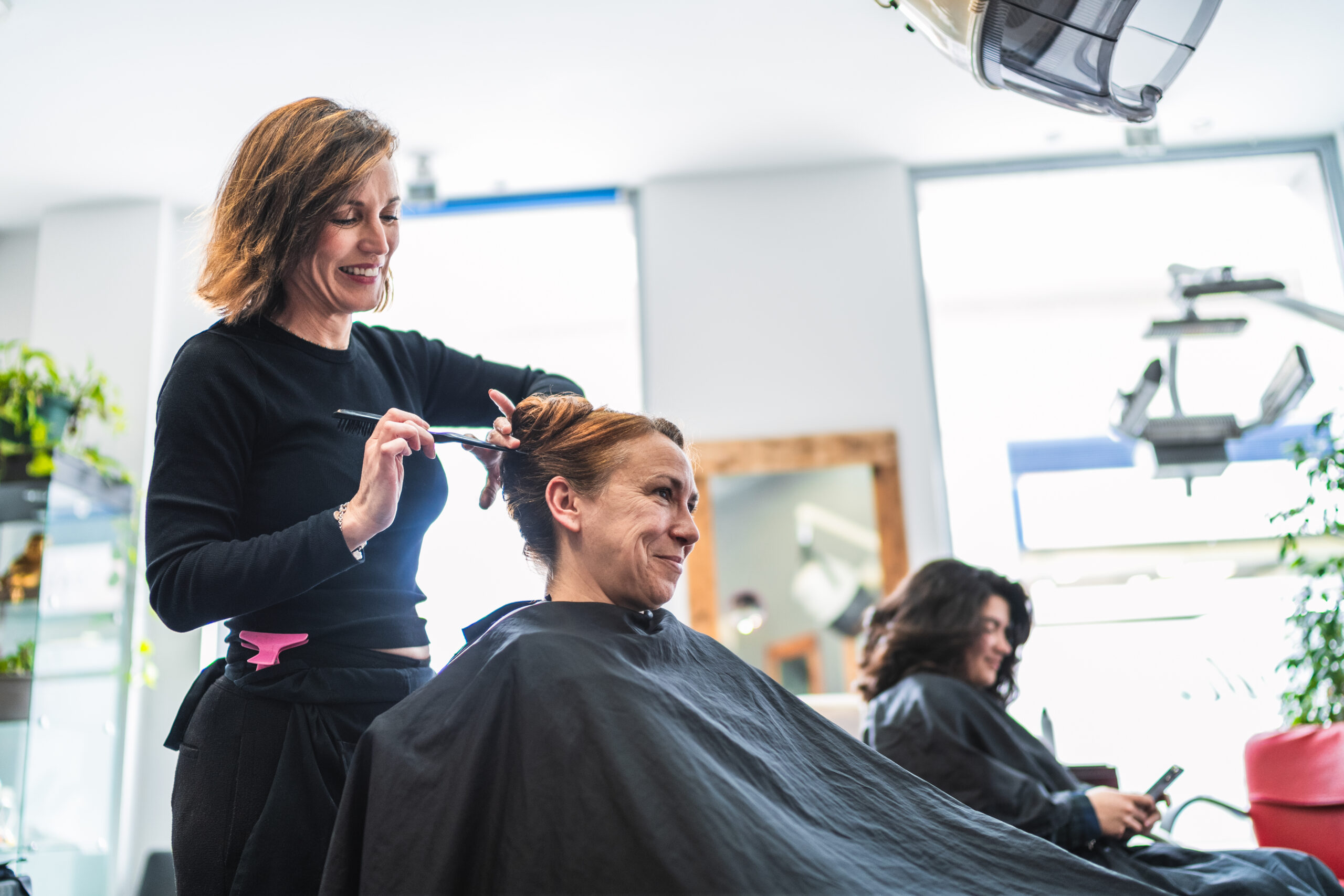 A hairdresser styles a client's hair in a modern salon, creating a neat bun. Concept of professional styling and client satisfaction.